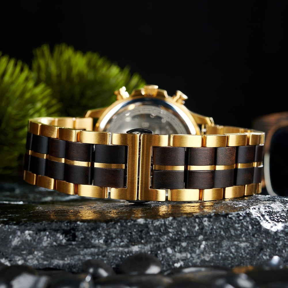 Back view of a luxury gold wristwatch with a black and gold link bracelet, showcasing the clasp and intricate details of the polished design, set against a dark, textured surface.