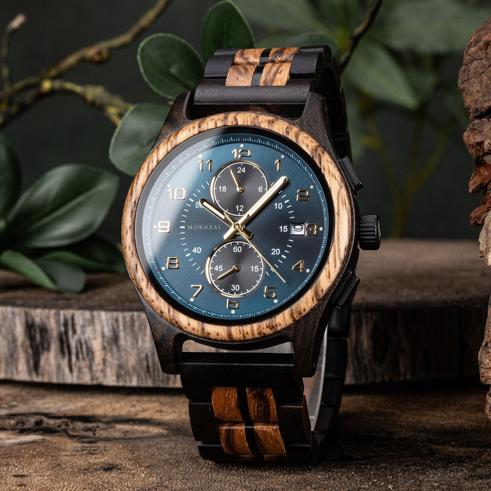 Mokozai wooden chronograph watch featuring a deep blue dial, gold accents, and natural wood grain bezel. The eco-friendly timepiece has a bold, black wood-accented strap, exuding luxury and craftsmanship, set against a natural, earthy backdrop.
