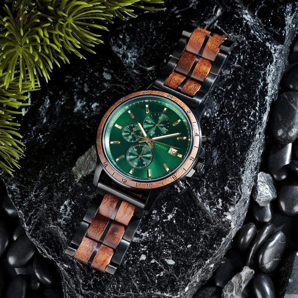 Luxurious Mokozai green-faced wooden chronograph watch with black and wood-link strap, displayed on dark stone surface with pine greenery.